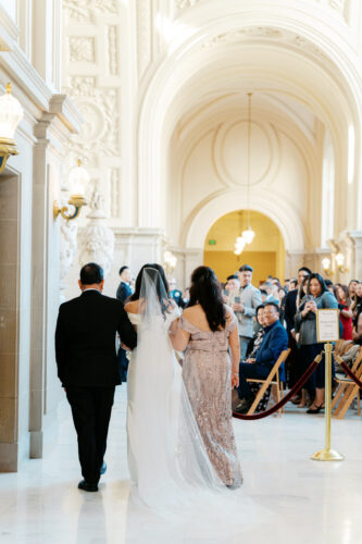 A bride enters her ceremony at the 4th floor at SF City Hall while her guests look at her in awe.