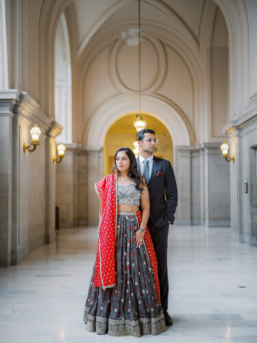 A couple at city hall wearing their traditional attire at city hall on the 4th floor balcony looking away from the camera
