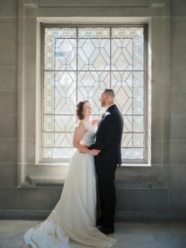 A beautiful couple takes a picture in front of one of the windows at city hall in San Francisco