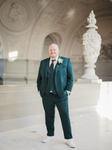 A portrait of a dashing groomsman in a green suit on the 4th floor balcony of city hall, san francisco