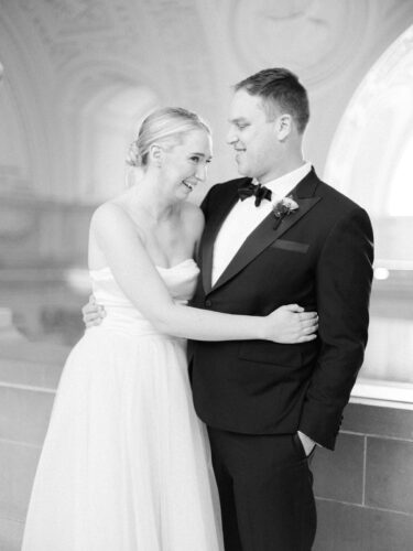 A couple smiling and laughing after their 4th floor balcony ceremony, captured by a San Francisco City Hall wedding photographer