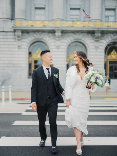 A stylish couple walks across the street in front of San Francisco City Hall captured by a San Francisco City Hall wedding photographer